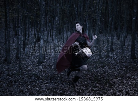 Woman dressed as Red Riding Hood running at night through the forest