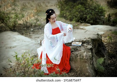 A woman dressed in traditional Chinese dress sat on a stone with a teapot and tea cup in her hands.Retro color card style