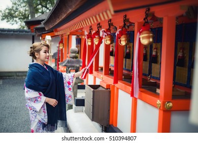 Woman dressed in traditional japanese costume (Kimono) walking under tori gates at the Fushimi-inari shrine, Kyoto Japan