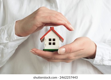 A woman dressed in a white shirt holds a small house in front of her - Powered by Shutterstock