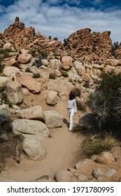 A Woman Dressed In White, Walking Through Rocky Steps On A Hike In Joshua Tree