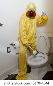 Woman dressed in yellow haz mat uniform and ventilator cleaning the bathroom toilet with scrub brush.