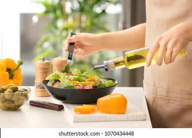 Woman dressing fresh vegetable salad with olive oil in kitchen - Powered by Shutterstock