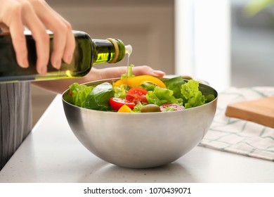 Woman Dressing Fresh Vegetable Salad With Olive Oil In Kitchen