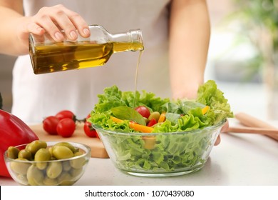 Woman Dressing Fresh Vegetable Salad With Olive Oil In Kitchen