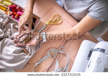 Woman dressmaker hands choosing thread color for sewing beige fabric clothes at workshop studio closeup. Female tailor fashion designer art work modist dressmaking professional occupation top view