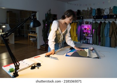 Woman dressmaker work late in studio choosing fabric samples for new clothes collection sewing. Female designer stay in workshop late busy with brand and small business development. Atelier ownership