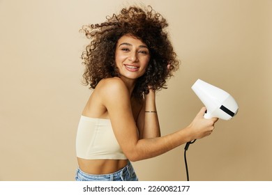 Woman dries curly afro hair with blow dryer, home beauty care styling products hair, smile on beige background - Powered by Shutterstock