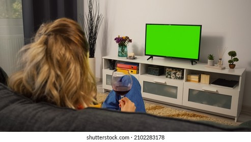 Woman Drink Red Wine Relaxing On A Living Room Couch While Watching Tv Greenscreen And Chroma Key. Mock Up With Tracking Markers And Alpha Matte. Over The Shoulder View.