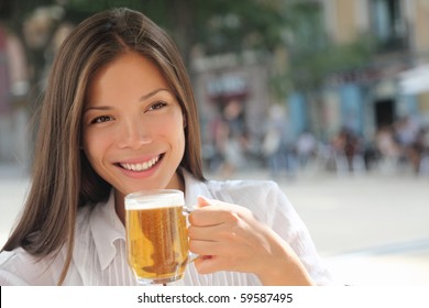 Woman drinking beer on sidewalk cafe. Beautiful young mixed race asian / caucasian female model smiling enjoying the city life at a town square.