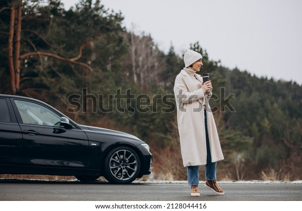 Woman drinking coffee by her car standing on the\
road in forest