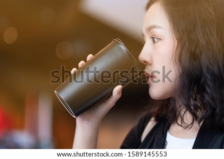 A woman drinking coffee by reuse black coffee bottle in coffee cafe 