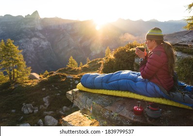 A woman drinking coffee from her bivouac on a beautiful morning in the mountains.