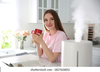 Woman drinking coffee in kitchen with modern air humidifier