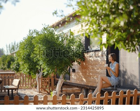 Woman is drinking coffee , morning routine near her Tiny house. First property. Small apartment in summer garden. Minimalism. Moving in. Living alone. Charming trailer house