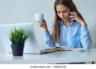 woman is drinking coffee at the office and is calling by phone.