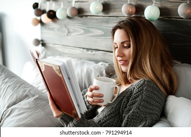 Woman Drinking Coffee And Reading Book On Bed 