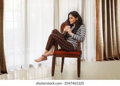 Woman drinking coffee and relaxing on armchair looking out from window