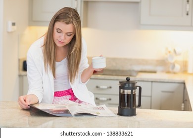 Woman drinking coffee while reading the newspaper in kitchen