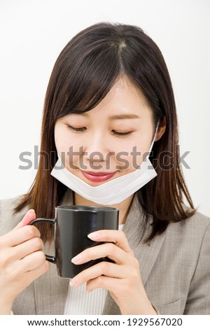 A woman drinking a drink with a mask on her chin