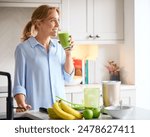 Woman Drinking Fresh Healthy Homemade Smoothie From Glass In Kitchen At Home