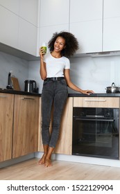 Woman Drinking Green Detox Juice, Smoothie Drink In Kitchen. Happy Smiling African Girl With Glass Of Healthy Fresh Raw Vegetable Smoothie At Home. Diet Nutrition Concept