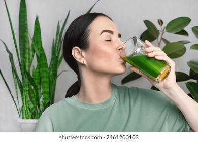 Woman drinking green healthy smoothie, drink. She drinks green wheatgrass energy shake. house interior with plants - Powered by Shutterstock