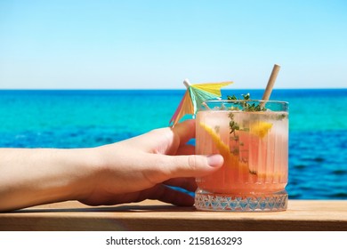Woman drinking hard seltzer cocktail at beach bar. Summer cocktail with grapefruit and thyme. 