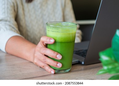 Woman drinking a homemade green detox juice. woman at work place drinkingGreen smoothie vegan spinach with avocado   Clean eating, alkaline diet, weight loss concept