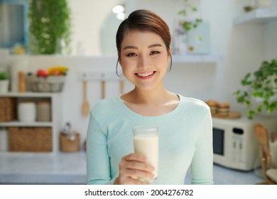 Woman Drinking Milk Looks Into Camera In Kitchen