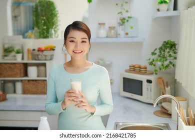 Woman Drinking Milk Looks Into Camera In Kitchen