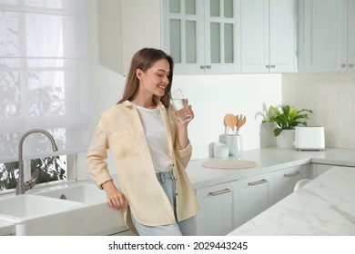 Woman drinking tap water from glass in kitchen - Shutterstock ID 2029443245