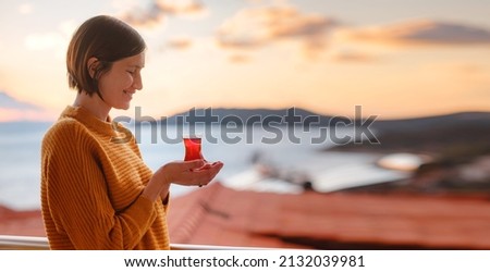 Woman drinking turkish tea from traditional turkish teacup and enjoys panorama over sunset of Kas resort town of Mediterranean sea in Turkey