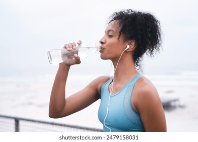 Woman, drinking water and exercise in outdoor for hydration, music and runner or workout break. Female person, profile and relax on promenade, cloudy sky and bottle of mineral liquid for nutrition - Powered by Shutterstock