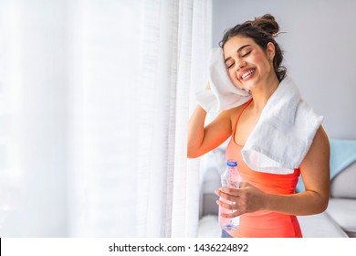 Woman drinking water at the home. Muscular woman taking break after exercise. Smiling attractive fitness woman with towel after training. Jogger run runner energy sweaty yoga vitality wellness concept