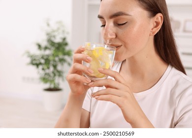 Woman drinking water with lemon indoors, closeup. Space for text - Powered by Shutterstock