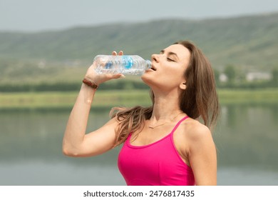 A woman is drinking water while standing by a lake. Concept of relaxation and rejuvenation, as the woman takes a break from her day to enjoy the natural beauty of the lake - Powered by Shutterstock