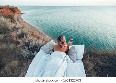 Woman Drinking Wine Enjoying View On Beach Landscape While Relaxing In Bed On Mountain In Sunset On The Edge Of Earth. Calm And Quiet Wanderlust Concept Moment When Person Feels Happiness And Freedom.