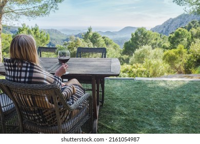 Woman Drinking Wine On The Terrace On A Sunny Day. Girl Enjoys Nature And Fresh Air In A Plaid.