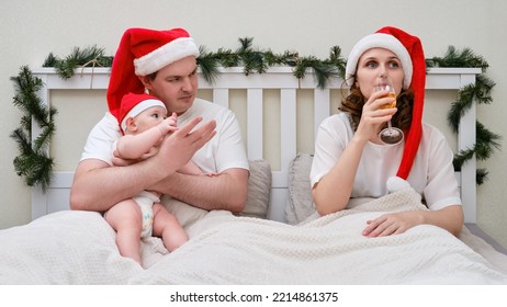 Woman Drinks Alcohol While A Man Sits With A Child In A Bed Decorated For Christmas And New Year, Family Couple In A Home Bedroom