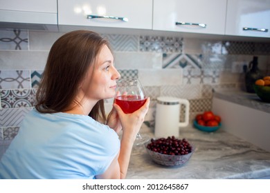 A Woman Drinks Wine Or Drink Alone In Her Kitchen At Home. Drinking Alcohol Alone. Glass Of Wine