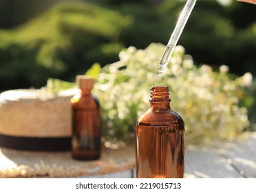 Woman Dripping Chamomile Essential Oil Into Bottle At White Table, Closeup. Space For Text