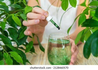 Woman Dripping Chlorophyll Supplement Into A Glass Of Water. Selective Focus. Drink.