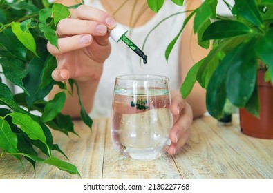 Woman dripping chlorophyll supplement into a glass of water. Selective focus. Drink.