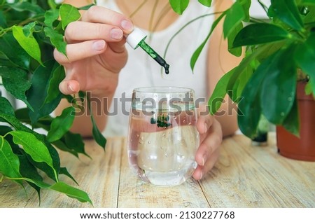 Woman dripping chlorophyll supplement into a glass of water. Selective focus. Drink.