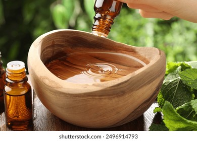 Woman dripping essential oil into wooden bowl of water on table, closeup - Powered by Shutterstock