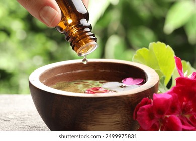 Woman dripping essential oil into wooden bowl of water on table, closeup - Powered by Shutterstock