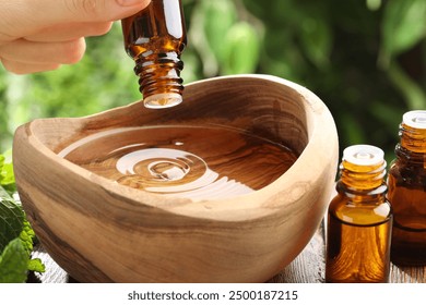 Woman dripping essential oil into wooden bowl of water on table, closeup - Powered by Shutterstock