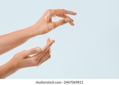 Woman with dripping honey on her hands against light background - Powered by Shutterstock