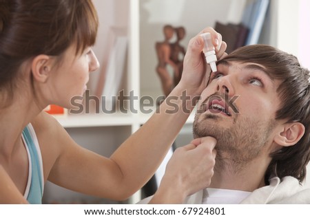 Woman dripping man eye with eyes drops